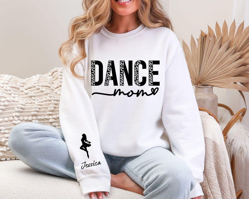 May include: White sweatshirt with the text "DANCE MOM" in black with a leopard print pattern. The sweatshirt has a black silhouette of a dancer on the left sleeve with the name "Jessica" underneath.