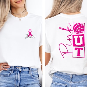 May include: White t-shirt with pink ribbon and the name "Jessica" on the front. The back of the shirt features the words "Pink Out" with a volleyball and ribbon graphic, supporting breast cancer awareness.