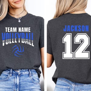 May include: Dark gray t-shirt with the words "TEAM NAME VOLLEYBALL FULL BALL" in white and blue, along with a volleyball graphic. The back of the shirt displays "JACKSON 12" in blue and white.