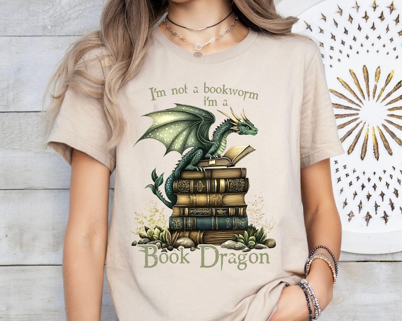 May include: A beige t-shirt with a green dragon sitting on a stack of books. The text on the shirt reads "I'm not a bookworm I'm a Book Dragon".