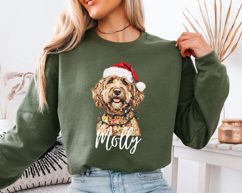 Pu&ograve; includere: Felpa verde oliva con un motivo festivo a forma di cane. Il cane indossa un cappello da Babbo Natale e luci natalizie. Il nome "Molly" &egrave; scritto in bianco. La felpa ha un girocollo e maniche lunghe.