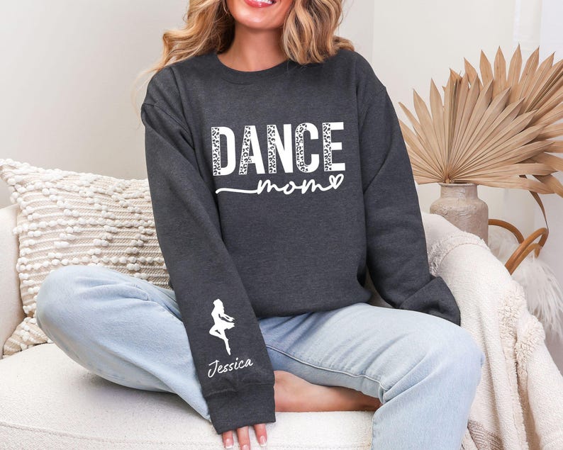 May include: A dark gray sweatshirt with the text "DANCE mom" in white with a leopard print pattern. The sweatshirt has a white silhouette of a dancer on the left sleeve with the name "Jessica" underneath.