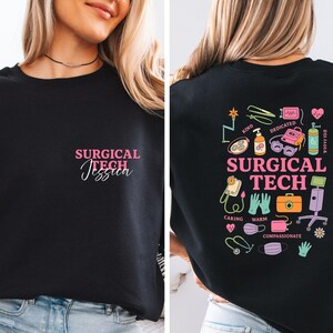May include: Black sweatshirt with the text "SURGICAL TECH Jessica" in pink on the front. The back of the sweatshirt features colorful medical-themed illustrations and the words "SURGICAL TECH".