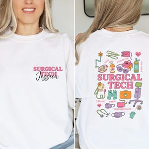 May include: White sweatshirt with the text "SURGICAL TECH Jessica" in pink and black script on the front. The back features colorful medical-themed illustrations and the words "SURGICAL TECH".