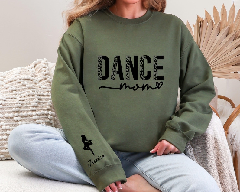 May include: Green sweatshirt with the text "Dance Mom" in black with a leopard print pattern. The sweatshirt has a small silhouette of a dancer on the left sleeve with the name "Jessica" underneath.