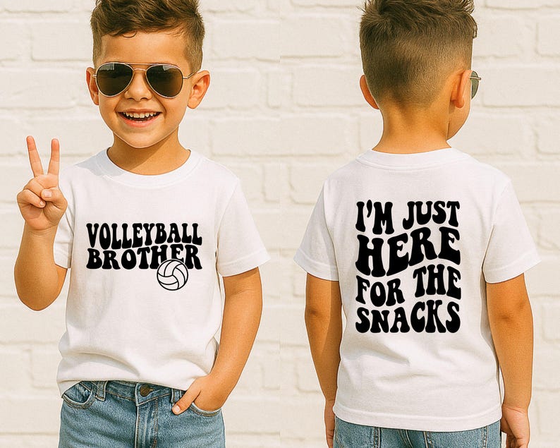 May include: A white t-shirt with the text "VOLLEYBALL BROTHER" and a volleyball graphic in black. The back of the shirt says "I'M JUST HERE FOR THE SNACKS" in black. The shirt is worn by a child.