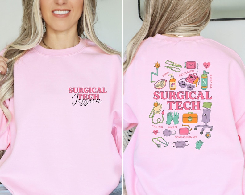 May include: A light pink sweatshirt with the text "SURGICAL TECH Jessica" on the front. The back of the sweatshirt features a colorful graphic with medical-related illustrations and the words "SURGICAL TECH".