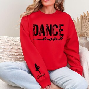 May include: Red sweatshirt with the text "Dance Mom" in black with a heart and a small dancer silhouette on the sleeve. The text is in a sparkly font.