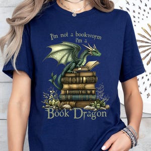 May include: A navy blue t-shirt with a green dragon sitting on a stack of books. The text "I'm not a bookworm I'm a Book Dragon" is printed on the shirt.