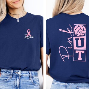 May include: Navy blue t-shirt with a pink ribbon and the name "Jessica" on the front. The back of the shirt features the words "Pink UT" with a volleyball graphic, also in pink. The shirt is a short-sleeved crew neck.