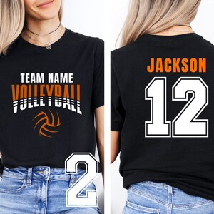 May include: Black volleyball team shirt with the text "TEAM NAME VOLLEYBALL" in white and orange. The shirt also features a volleyball graphic and the number "12" with the name "JACKSON" on the back.