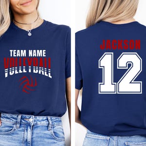May include: Navy blue t-shirt with the words "TEAM NAME VOLLEYBALL FULLL BALL" in white and red. The back of the shirt has the name "JACKSON" in red above the number "12" in white.