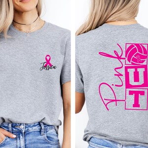 May include: A heather gray t-shirt with a pink ribbon and the name "Jessica" printed on the front. The back of the shirt features the words "Pink UT" with a volleyball graphic, all in pink. The shirt is a casual style.