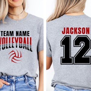 May include: A heather gray volleyball t-shirt with the words "TEAM NAME VOLLEYBALL" in black and red, and a volleyball graphic. The back of the shirt displays "JACKSON 12" in black and red.