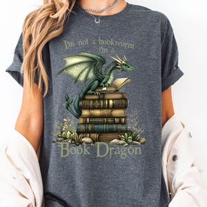 May include: A gray t-shirt with a green dragon sitting on a stack of books. The text on the shirt reads "I'm not a bookworm I'm a Book Dragon".