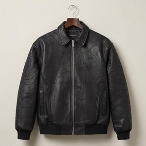 Puede incluir: Una chaqueta bomber de cuero negro con un patrón de telaraña en relieve tono sobre tono en la parte delantera y las mangas. La chaqueta incluye un cuello clásico, una cremallera metálica plateada, dos bolsillos laterales y puños y dobladillo acanalados negros.