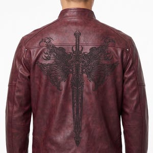 Op de afbeelding: Een donkerrode leren jas met een opstaande kraag en een grote, gedetailleerde zwarte grafische print op de achterkant. Het ontwerp toont een gedetailleerd zwaard omringd door sierlijke, vleugelachtige patronen. De jas heeft lange mouwen.