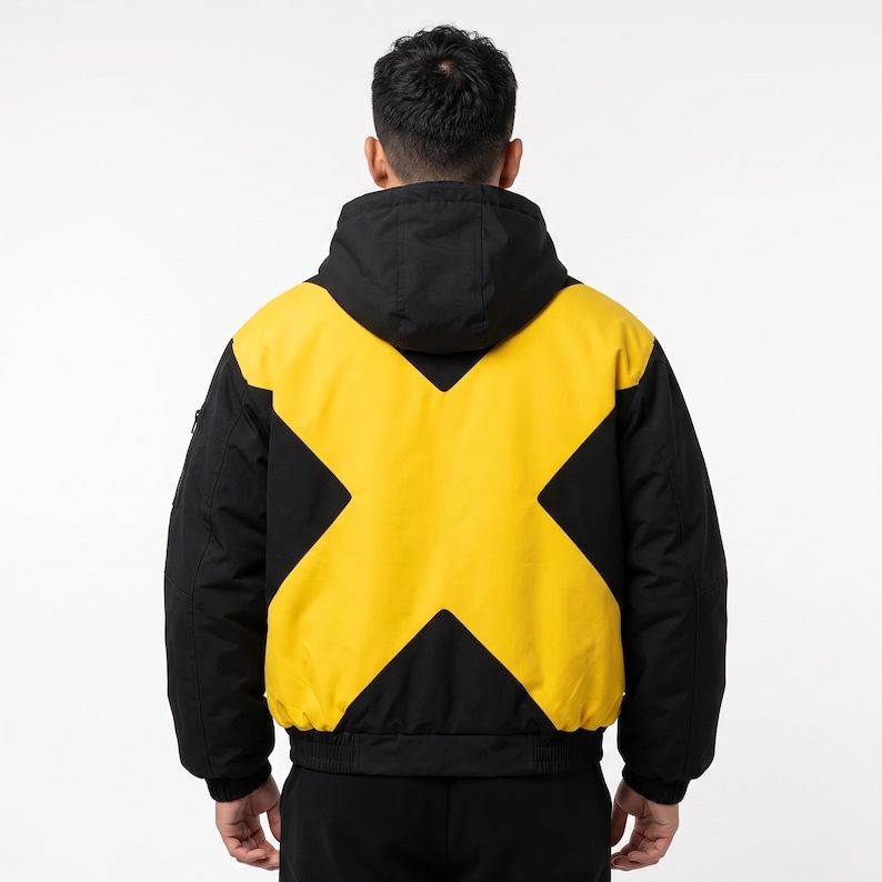 May include: A hooded jacket featuring a bold yellow X-shaped graphic across the back, set against a solid black background. The garment includes a black hood, long sleeves, and a ribbed hem, showcasing a high-contrast color-blocked design.