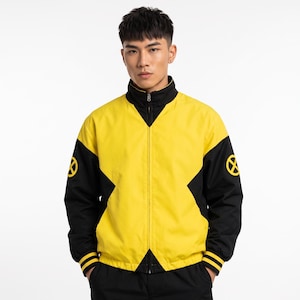 May include: A yellow and black zip-up jacket featuring a high collar and long sleeves with ribbed cuffs. The design includes a prominent black X-shaped pattern across the chest and back, with a yellow circular X logo on each sleeve.