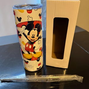 Puede incluir: Un vaso de acero inoxidable blanco con un dise&ntilde;o de Mickey Mouse. El vaso tiene una imagen de Mickey Mouse roja, amarilla y negra. El vaso viene con una pajita y una caja blanca.