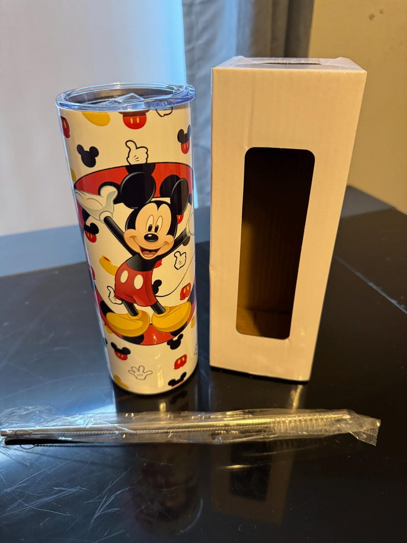 Puede incluir: Un vaso de acero inoxidable blanco con un dise&ntilde;o de Mickey Mouse. El vaso tiene una imagen de Mickey Mouse roja, amarilla y negra. El vaso viene con una pajita y una caja blanca.