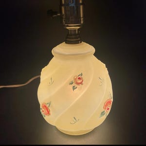 May include: A white ceramic table lamp with a swirl design and painted pink roses. The lamp has a metal base and a white cord.