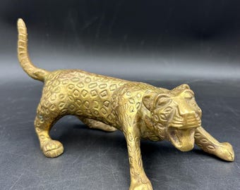 May include: A brass leopard figurine in a stalking pose. The sculpture has a textured surface with a spotted pattern. The leopard's mouth is slightly open, and its tail is raised. The figurine is a decorative item.