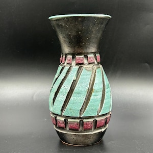 May include: A ceramic vase with a black top and base, a turquoise center with diagonal lines, and maroon accents. The vase has a textured surface and a flared top. The vase is approximately 8 inches tall.