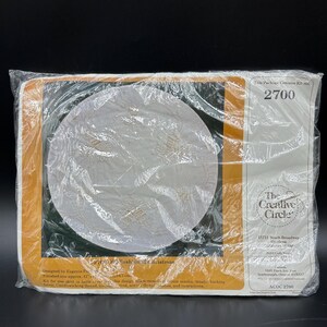 May include: A sealed plastic package containing a craft kit for a tree skirt or table cover, kit number 2700 by The Creative Circle. The package features a circular white fabric piece with a printed design and lists a finished size of 41 inches.