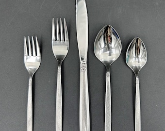 May include: A set of five silver-colored flatware pieces, including a knife, two forks, and two spoons. The knife has a decorative handle, and all pieces have a textured design on the handles. The flatware is arranged on a dark surface.