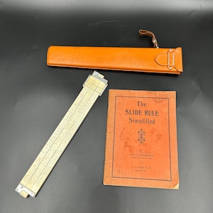 May include: An antique slide rule with a leather case and a book titled "The Slide Rule Simplified." The slide rule is off-white with black markings. The book has an orange cover with black text. The leather case is orange.