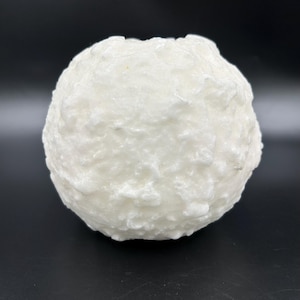May include: A spherical, off-white object with a textured, uneven surface. The object appears to be made of a solid material, possibly ceramic or a similar substance. The shape is roughly round, with no visible features or markings.