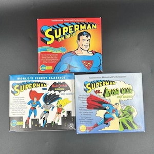 May include: Three vintage Superman radio show CD sets. The boxes are red, blue, and white, featuring illustrations of Superman and other characters. The text on the boxes reads "Superman on Radio" and "World's Finest Classics."