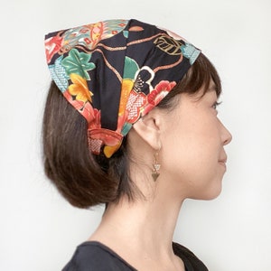 May include: A woman with short black hair is wearing a black and floral patterned headband. The headband has a gold rope design and is tied in a knot at the back of her head. She is wearing gold triangle earrings.