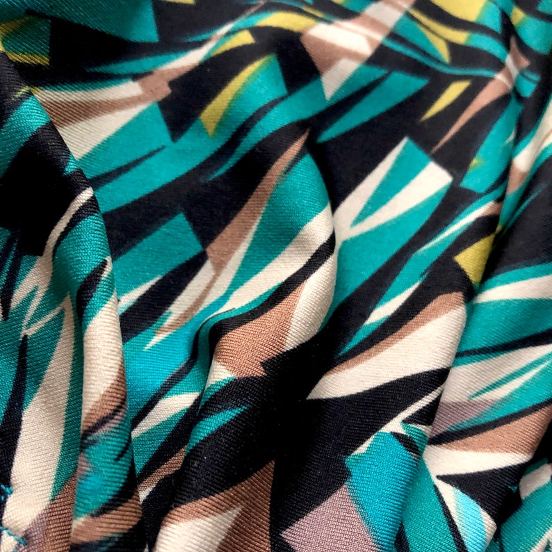 Puede incluir: Tela de estampado geom&eacute;trico abstracto en colores turquesa, negro, blanco y marr&oacute;n. La tela es suave y tiene una textura lisa.