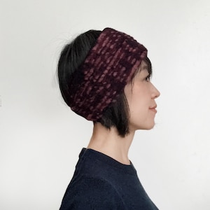 May include: A burgundy and mauve knitted headband. The wide, textured headband is worn on the head, covering the ears and forehead. The accessory is made of a soft, warm material, ideal for cold weather.