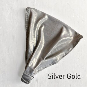 May include: A silver and gold metallic fabric headband. The headband is folded and has a seam around the edge.