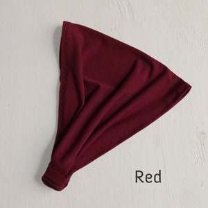 May include: A red fabric headband, folded and ready to wear. The headband is made of a soft, stretchy material.