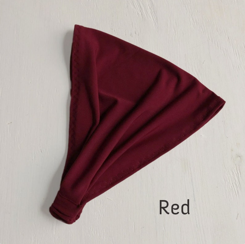 May include: A red fabric headband, folded and ready to wear. The headband is made of a soft, stretchy material.