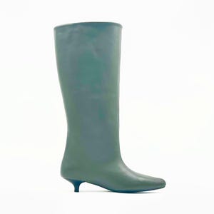 May include: A tall, olive-green boot with a pointed toe and a small, black heel. The boot has a smooth, matte finish and a streamlined design. The shaft of the boot extends to the mid-calf. The boot is set against a white background.