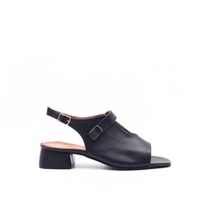 May include: Black leather sandal with a square toe and a small, block heel. The sandal features an adjustable ankle strap and a strap across the top of the foot. The shoe has a minimalist design.