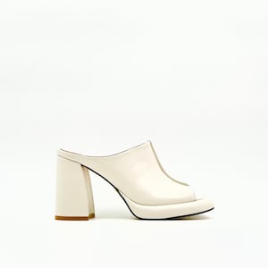 May include: Cream-colored open-toe platform mules with a chunky heel. The heel is approximately 4 inches tall. The shoe has a rounded toe and a smooth, leather-like finish. The sole is black.