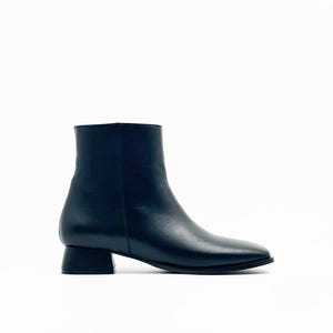 Puede incluir: Botín negro con punta cuadrada y tacón de bloque pequeño. La bota tiene una textura de cuero liso y un diseño simple y moderno. La bota mide aproximadamente 15 cm de alto.