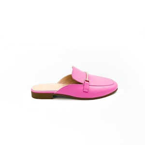 May include: Pink leather mule with a gold buckle. The shoe has a low heel and a pointed toe.