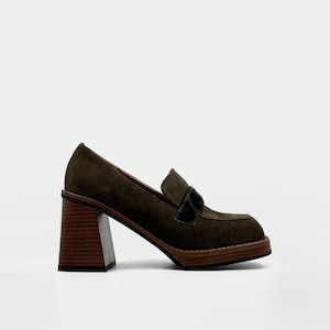 Könnte beinhalten: Olivgrüner Loafer mit Absatz aus Wildleder mit eckiger Spitze und einem dunkelbraunen Holzblockabsatz. Der Schuh hat einen dunklen Samtakzent auf dem Blatt und eine Holzsohle.