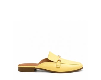 May include: A pale yellow backless loafer mule featuring a smooth finish, a rounded toe, and a gold-toned metal horsebit detail across the vamp. The shoe has a low, flat brown heel and a tan interior lining, presented from a side profile view.