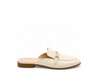 May include: A cream-colored backless loafer mule featuring a smooth finish, a rounded toe, and a gold-toned metal horsebit detail across the vamp. The shoe has a low, flat brown heel and a light-colored interior lining.
