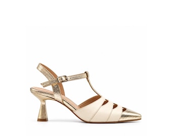 Puede incluir: Un zapato de pulsera en T dorado y crema con punta afilada, acabado dorado metálico en el tacón y la puntera, y una correa de tobillo con hebilla. El zapato presenta un diseño con aberturas laterales y un tacón de carrete acampanado.