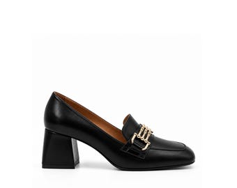 Könnte beinhalten: Ein schwarzer Leder-Loafer mit quadratischer Zehenpartie und Blockabsatz. Der Schuh verfügt über ein goldfarbenes Metalldetail auf dem Vorderblatt, das aus drei horizontalen Stäben besteht, die durch vertikale Glieder verbunden sind.