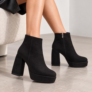 May include: A pair of black ankle boots featuring a high block heel and a platform sole. The boots have a smooth, matte finish and a side zipper closure. The design includes a rounded toe and a structured silhouette that reaches above the ankle.